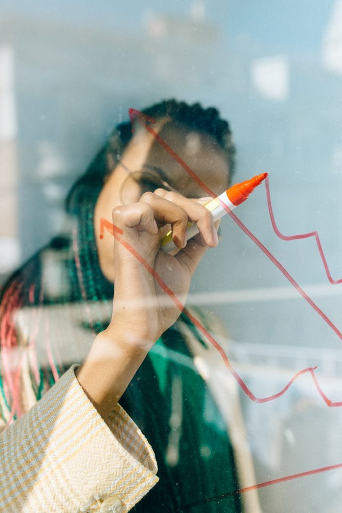 A businesswoman draws a red financial graph on a glass panel, symbolizing strategy and success.